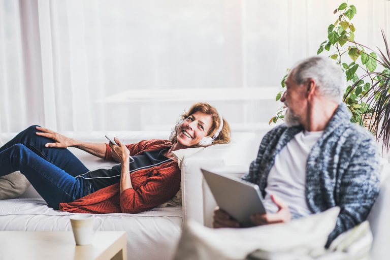 A Relaxed Adult Couple At Home Looking At A Tablet And Listening To Music