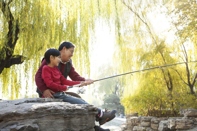 A Grandfather And Grandson Smiling While They Go Fishing Together