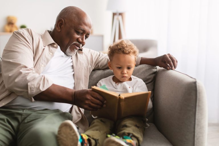 A Grandparent Helps Their Grandchild Read A Book, Representing A Family Legacy.