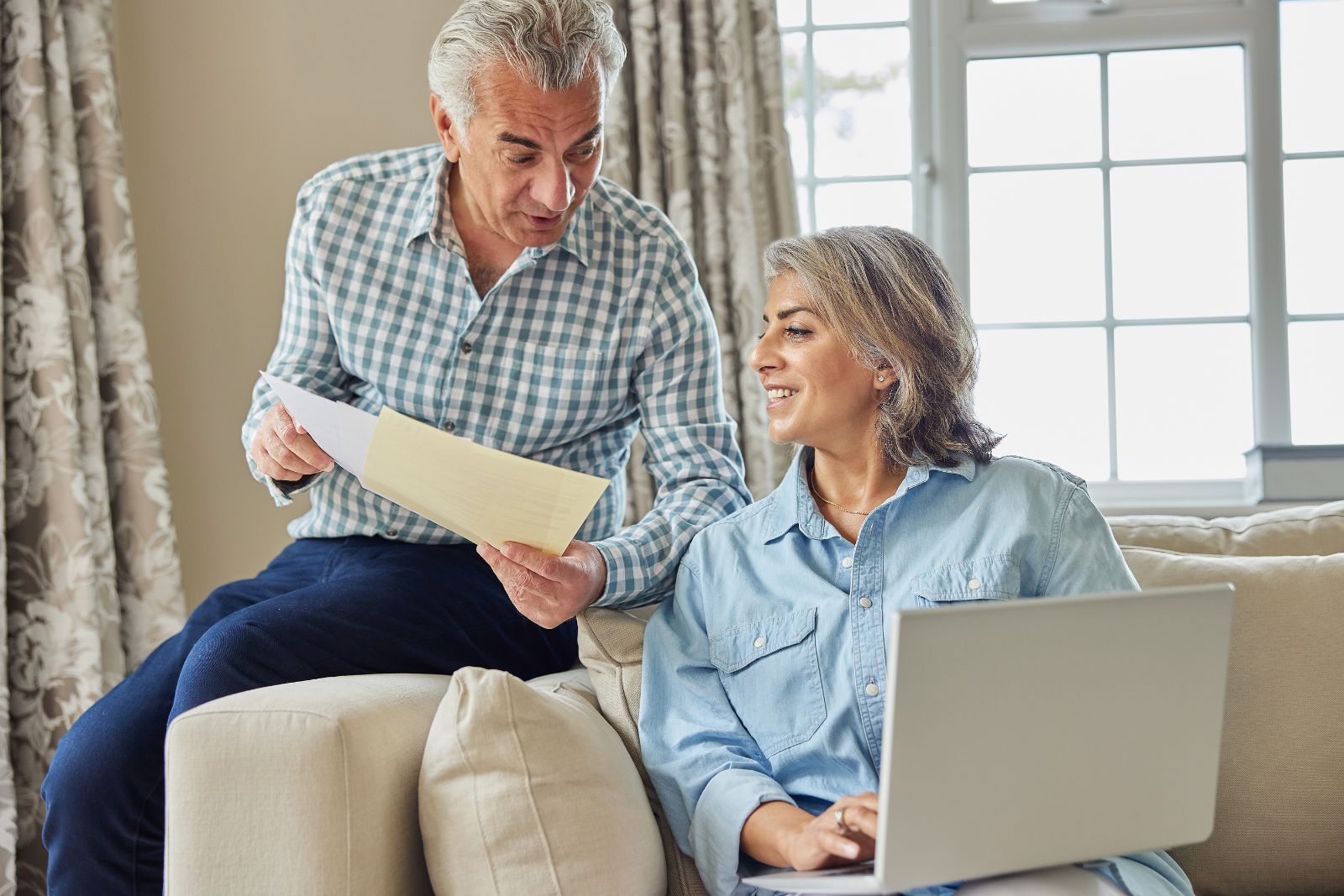 Older couple reviewing documents on a laptop in a bright living room while planning their digital estate
