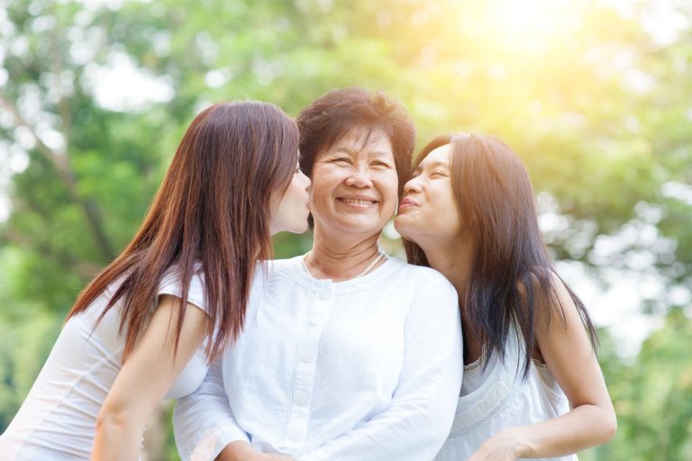 Two adult children kiss their parent on the cheek